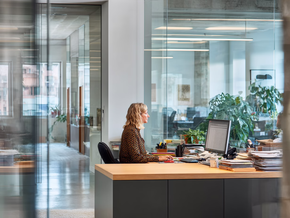 Accounting firm administrator working at a desk in a modern office, with client files stacked beside her monitor
