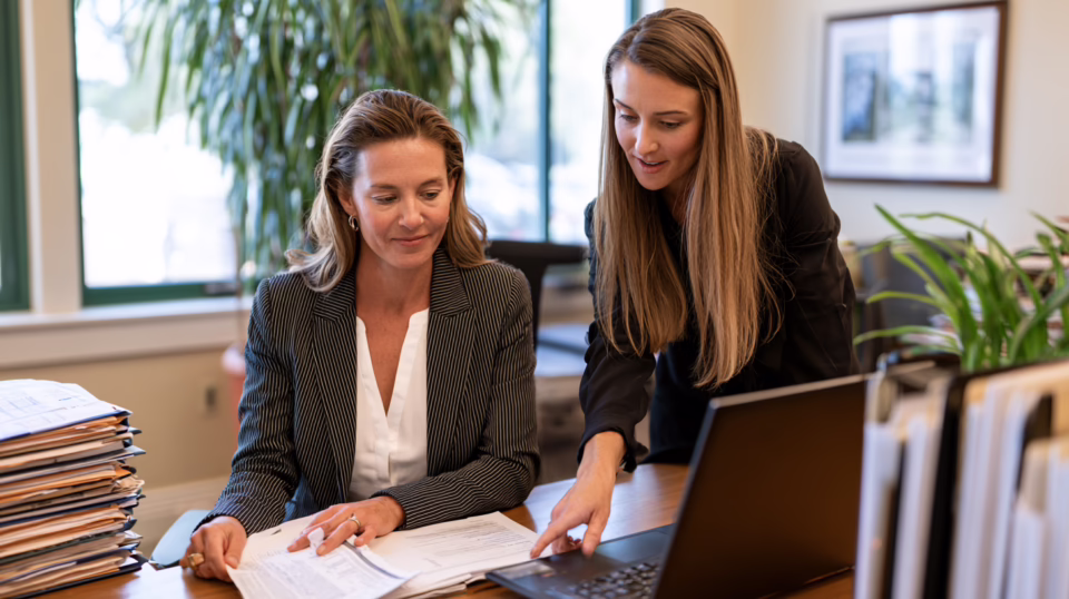 Two accounting professionals at a CPA firm reviewing a client's tax preparation documents together at a laptop.